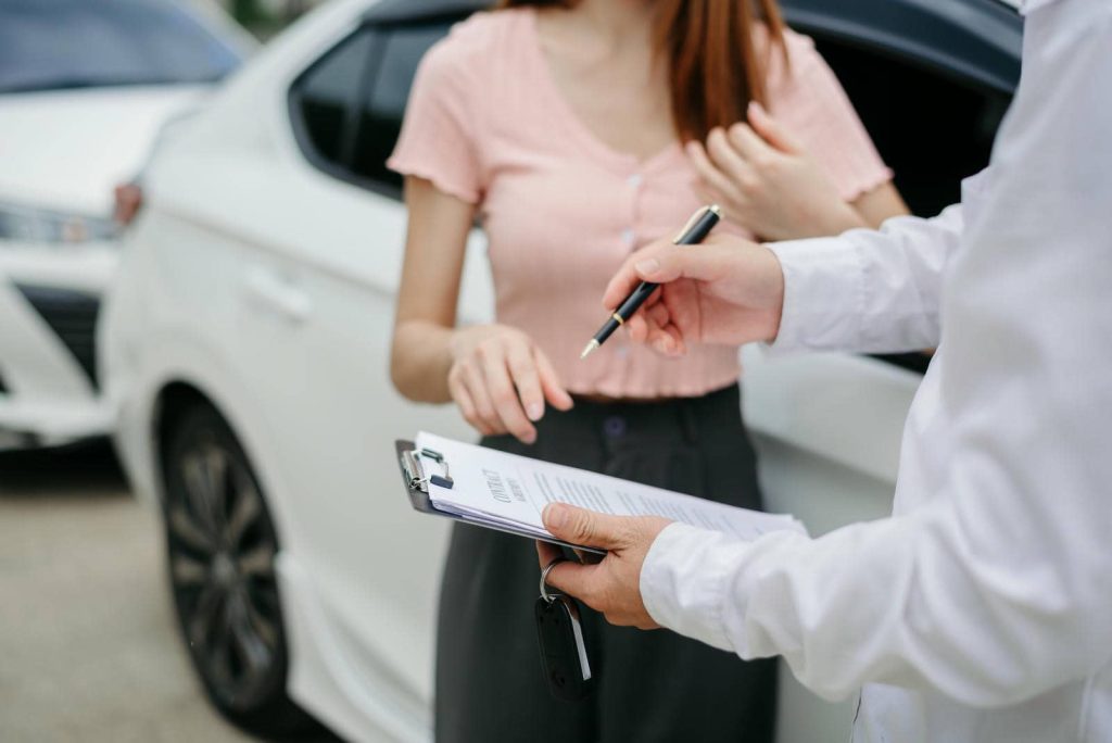 Insurance companies for accident claims processing man signing papers with car in background